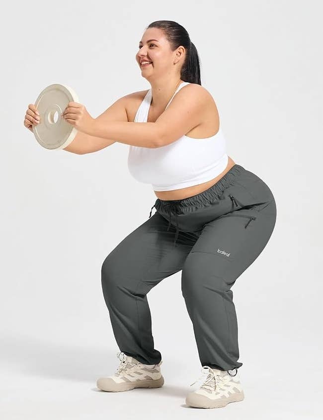 Person exercising with a value   disc, wearing a achromatic  sports bra and grey  workout pants, smiling successful  a workout setting