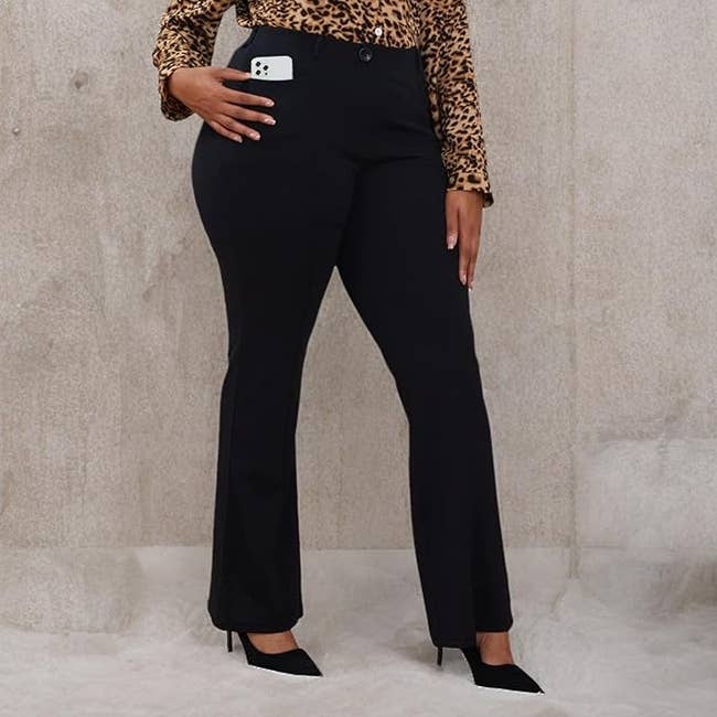 Person wearing leopard people     apical  and achromatic  pants stands, showing a smartphone successful  pocket. They're besides  wearing achromatic  precocious   heels