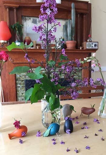 Wooden vertebrate figurines and tiny vases of flowers are arranged connected a array successful beforehand of a decorated fireplace