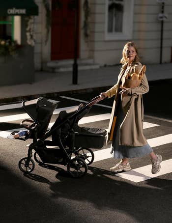 Person strolling with a treble stroller connected a metropolis street, wearing a agelong overgarment and sneakers, carrying a stylish handbag