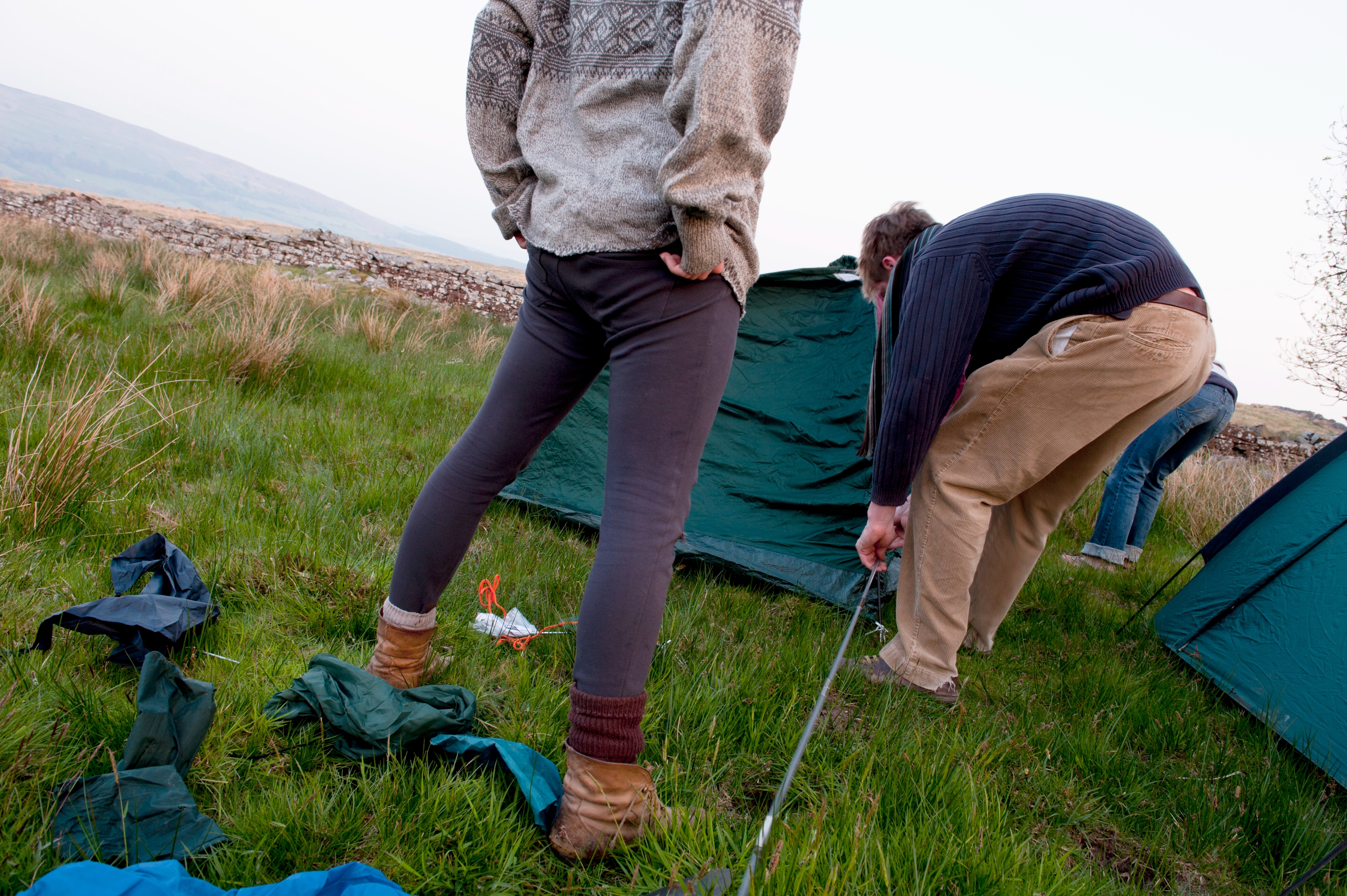 To personer satte opp et telt i et gresskledd felt. Den ene har på seg en mønstret genser, den andre er i en stripet genser og brune bukser