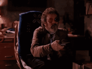 A person wearing 3D glasses sits on a chair and uses a TV remote, appearing engaged with what&#x27;s on screen