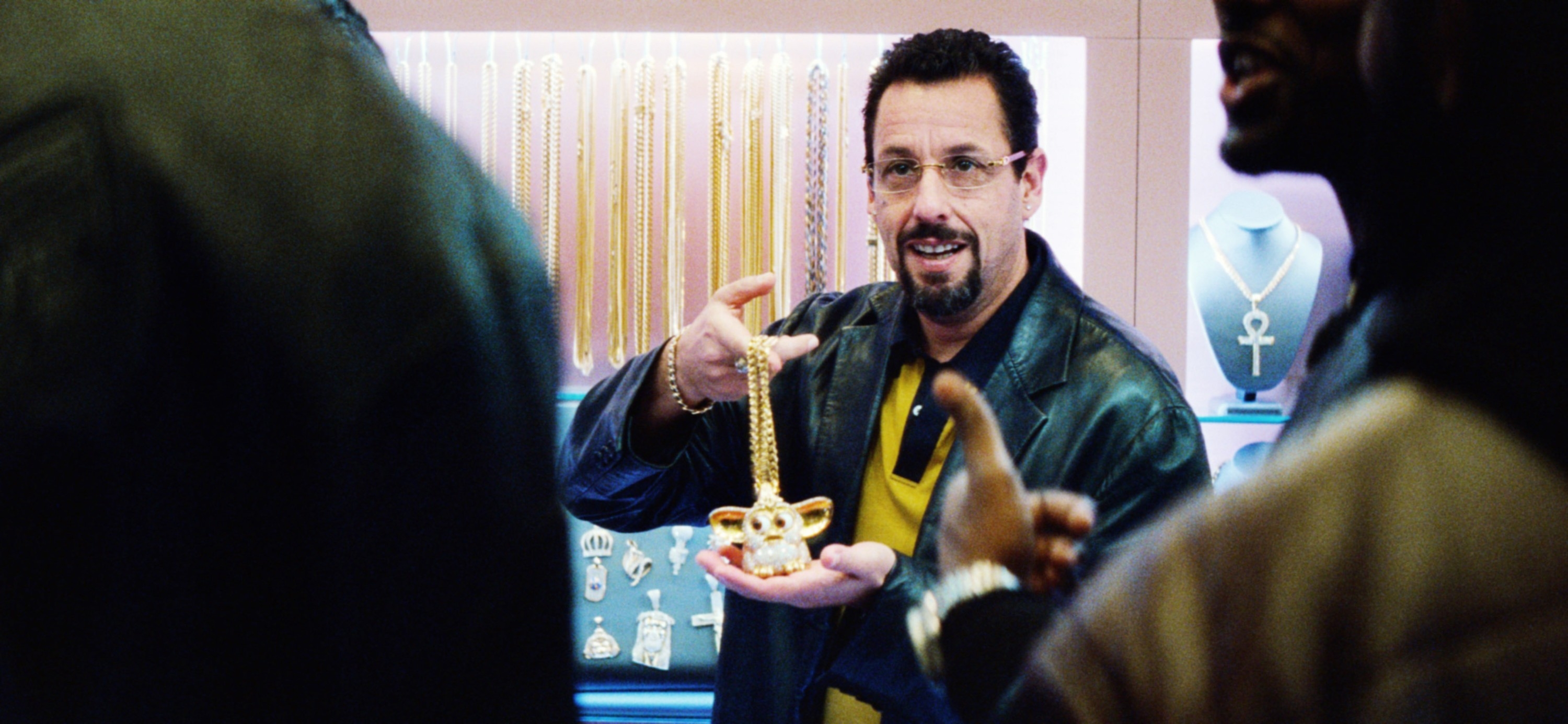 Man in a leather jacket holds a gold pendant in a jewelry store, engaging with two people nearby
