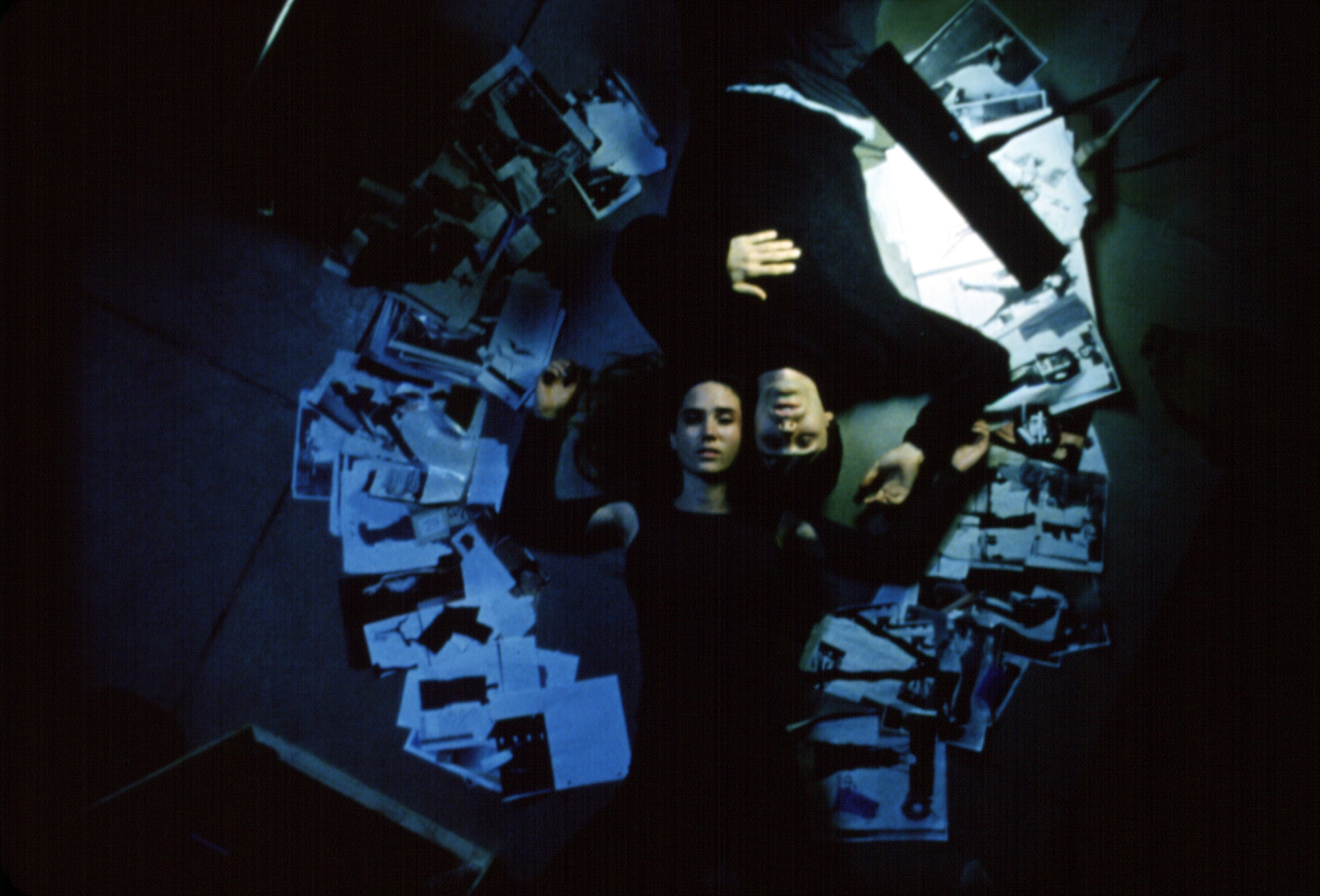 Two people lie on the floor surrounded by scattered photographs, appearing contemplative or engaged in a quiet moment together