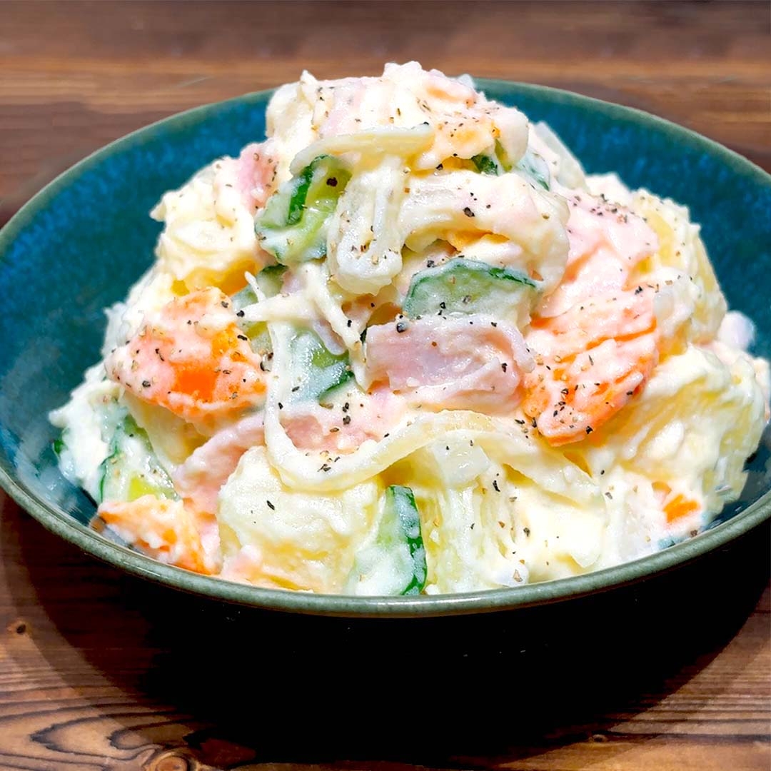 クリーミーなポテトサラダが青い皿に盛られ、黒コショウが振りかけられている。野菜が混ざっている。