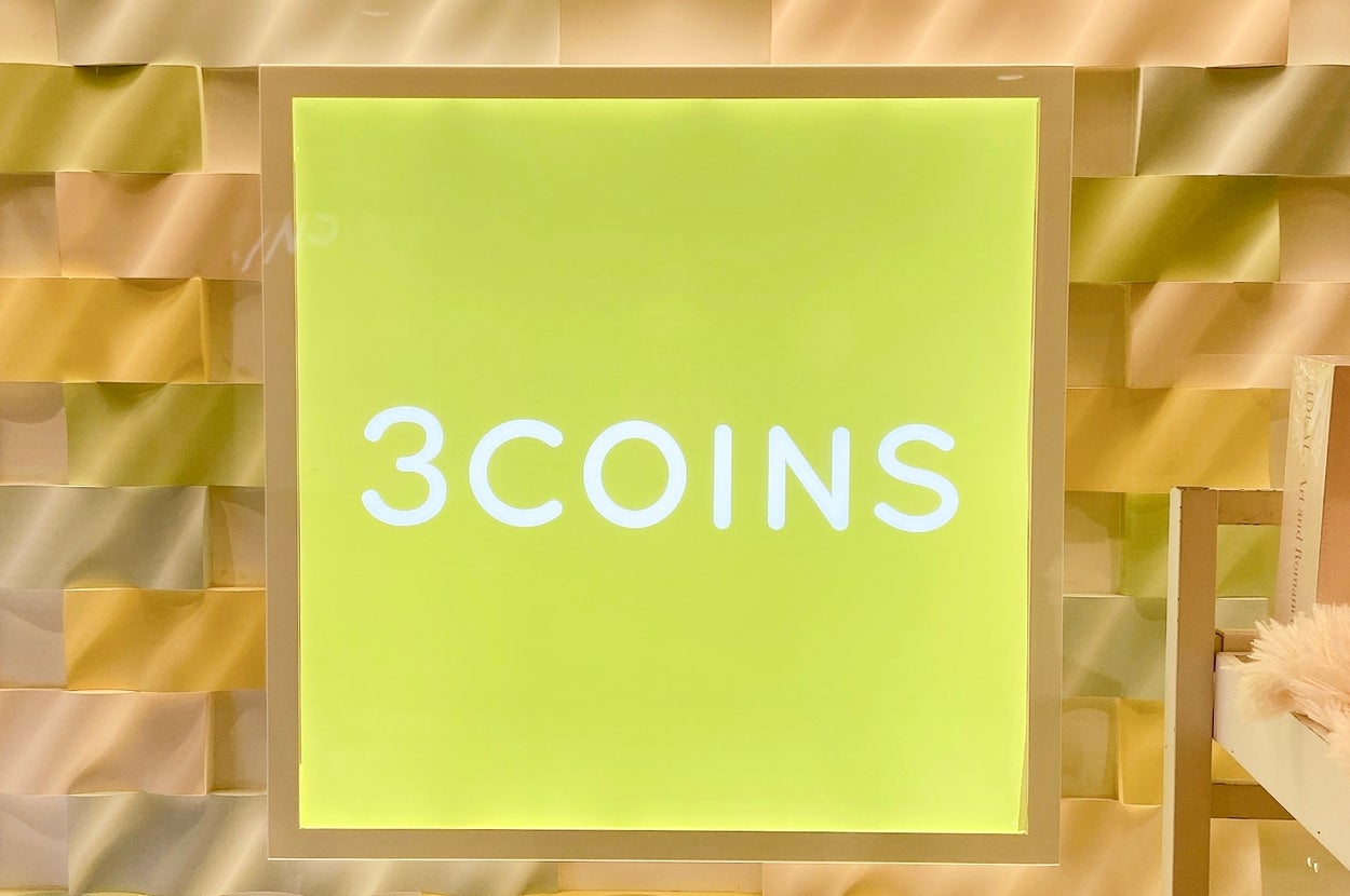 「3COINS」の広告看板が室内の壁に掛かっている様子。