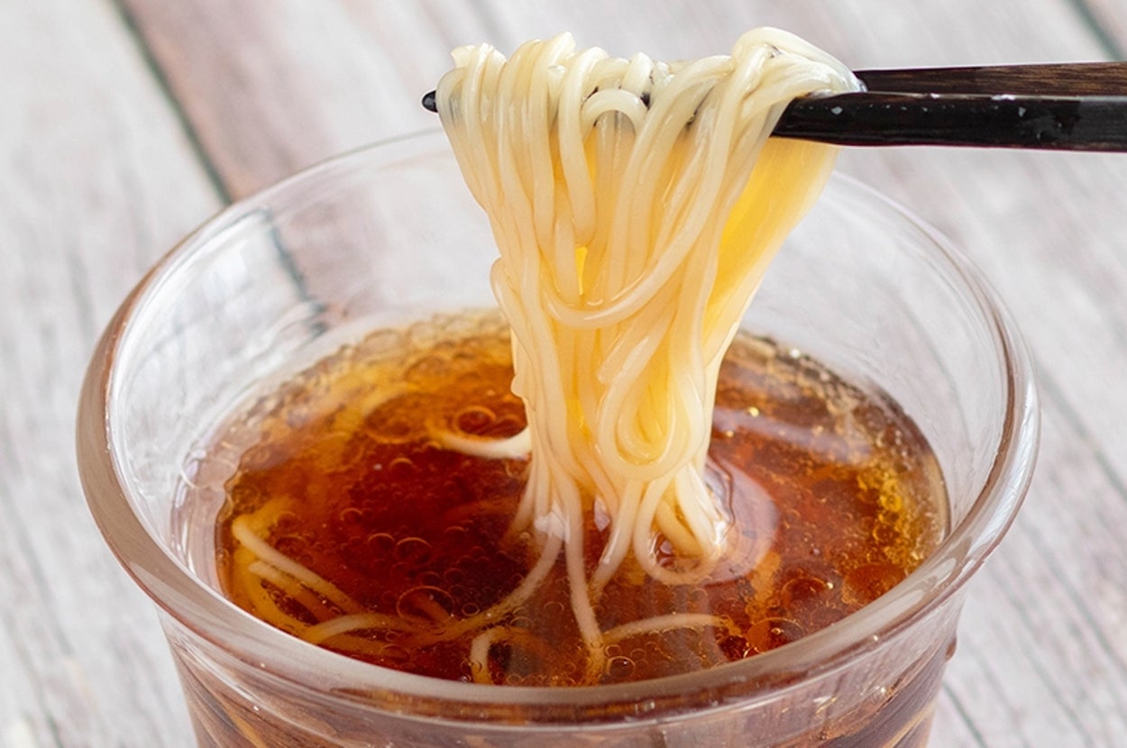 ガラスのカップに盛られた麺を箸で持ち上げている。カップにはつゆが入っている。