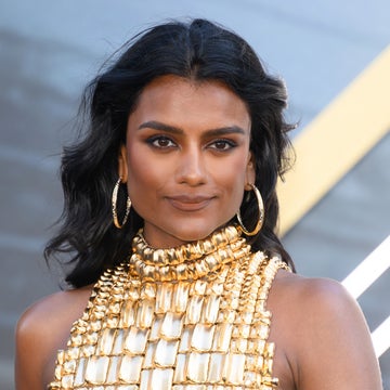 Person in sleeveless dress with textured pattern, wearing large hoop earrings, standing in front of a backdrop