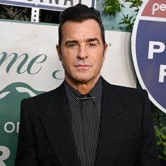 Man in a suit with pinstriped shirt standing in front of signs at a TV event