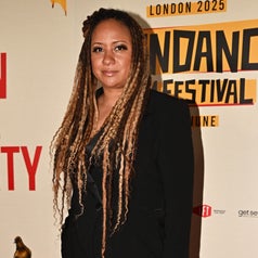 Individual with long braids in a stylish black suit stands in front of a backdrop for a film festival