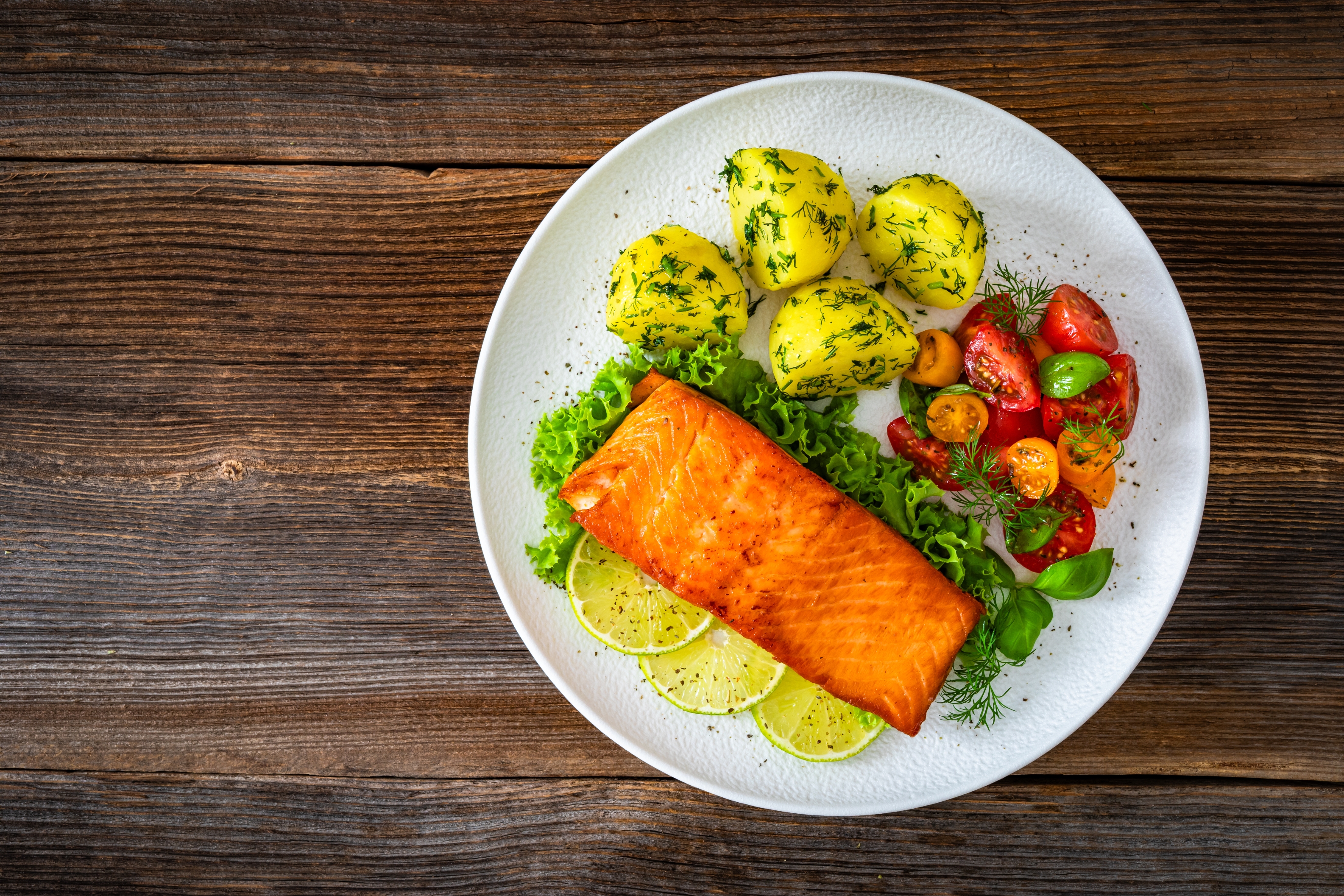 Grillet laksefilet servert med sitronskiver, dillpoteter og kirsebærtomatsalat på en hvit tallerken