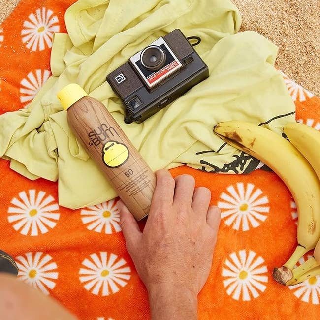 Sunscreen bottle, vintage camera, and bananas connected an orangish daisy-patterned blanket, suggesting a formation time theme