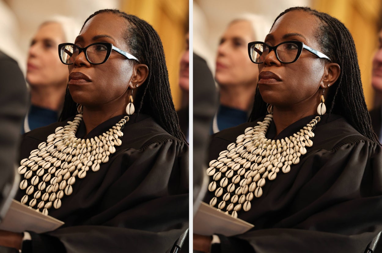 A person with glasses and long braids is wearing a decorative shell necklace and earrings, attending a formal event