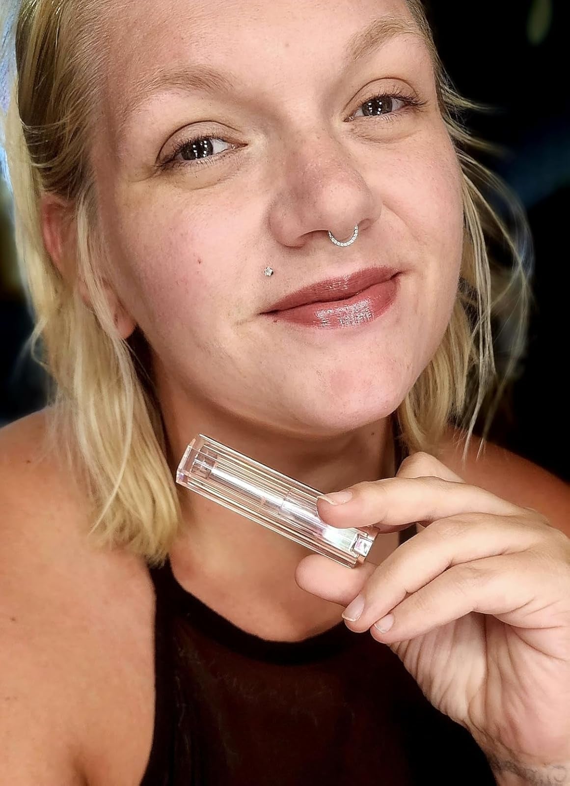 Person holding a wide   lipstick tube, smiling astatine  the camera, successful  close-up