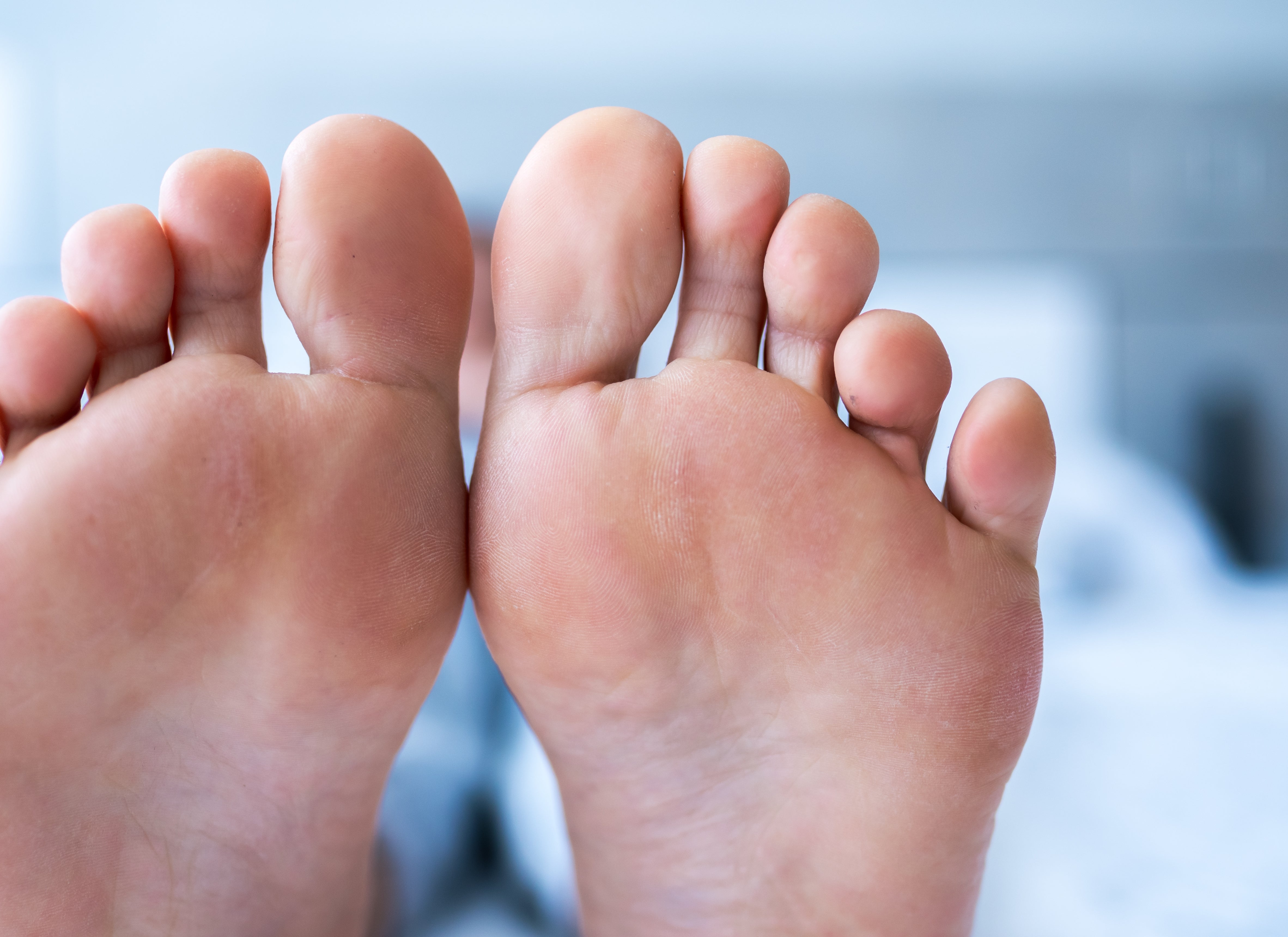 Nærbilde av to bare føtter side om side, tær vendt mot kameraet, hviler på en seng med uskarpt bakgrunn