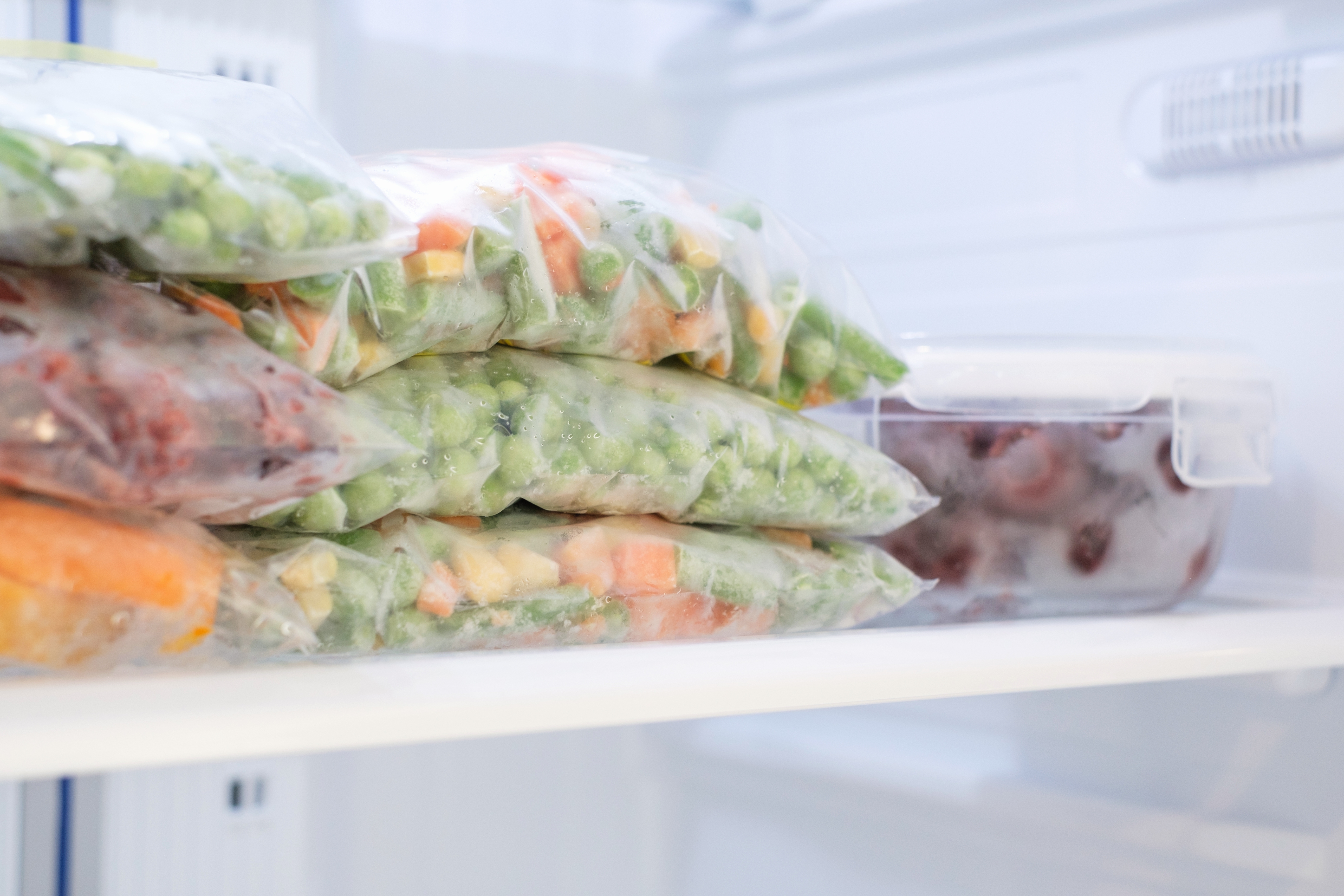 Poser med diverse frosne grønnsaker er stablet pent i en fryser