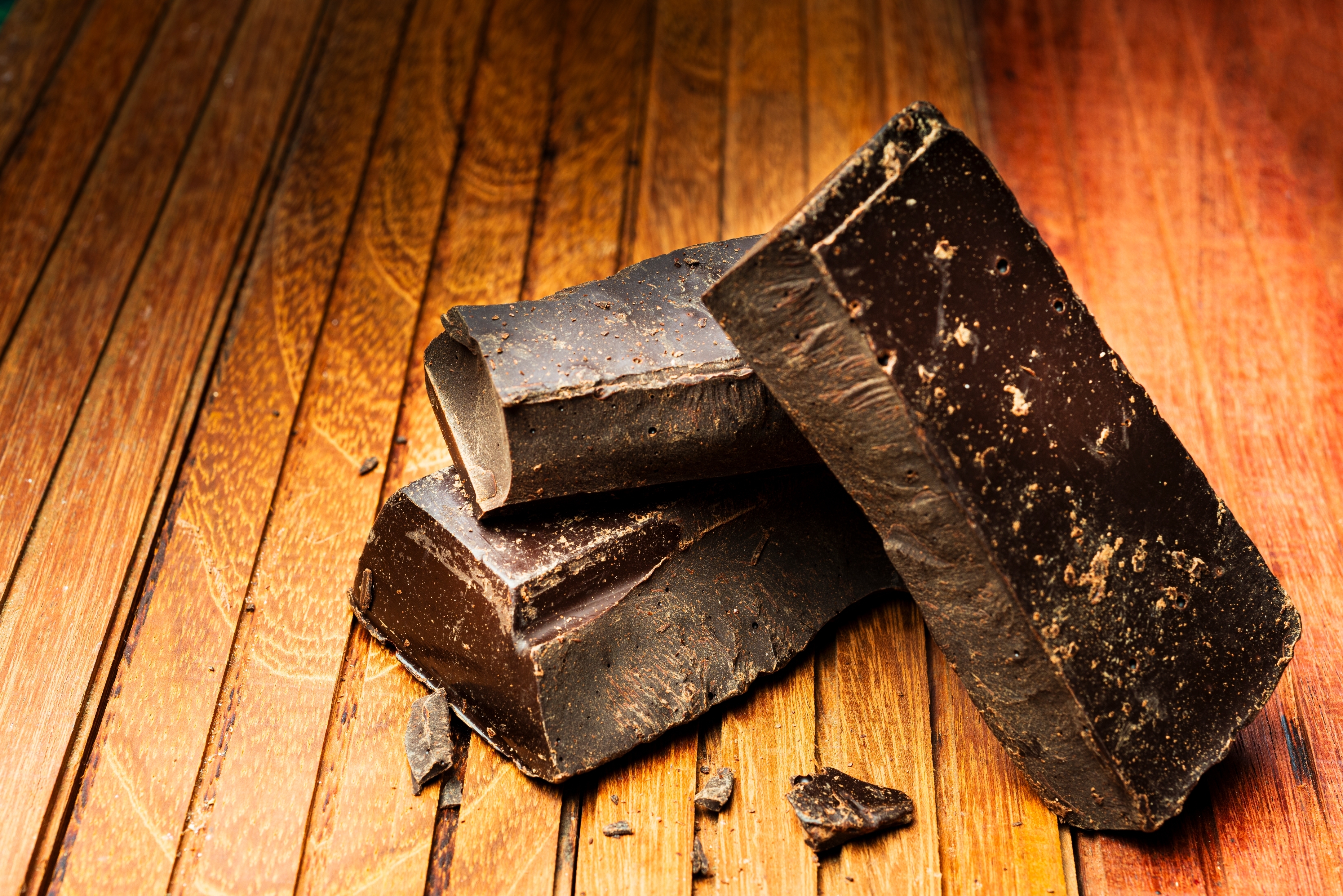 Tre store biter av mørk sjokolade på en treoverflate, med synlig tekstur og detaljer