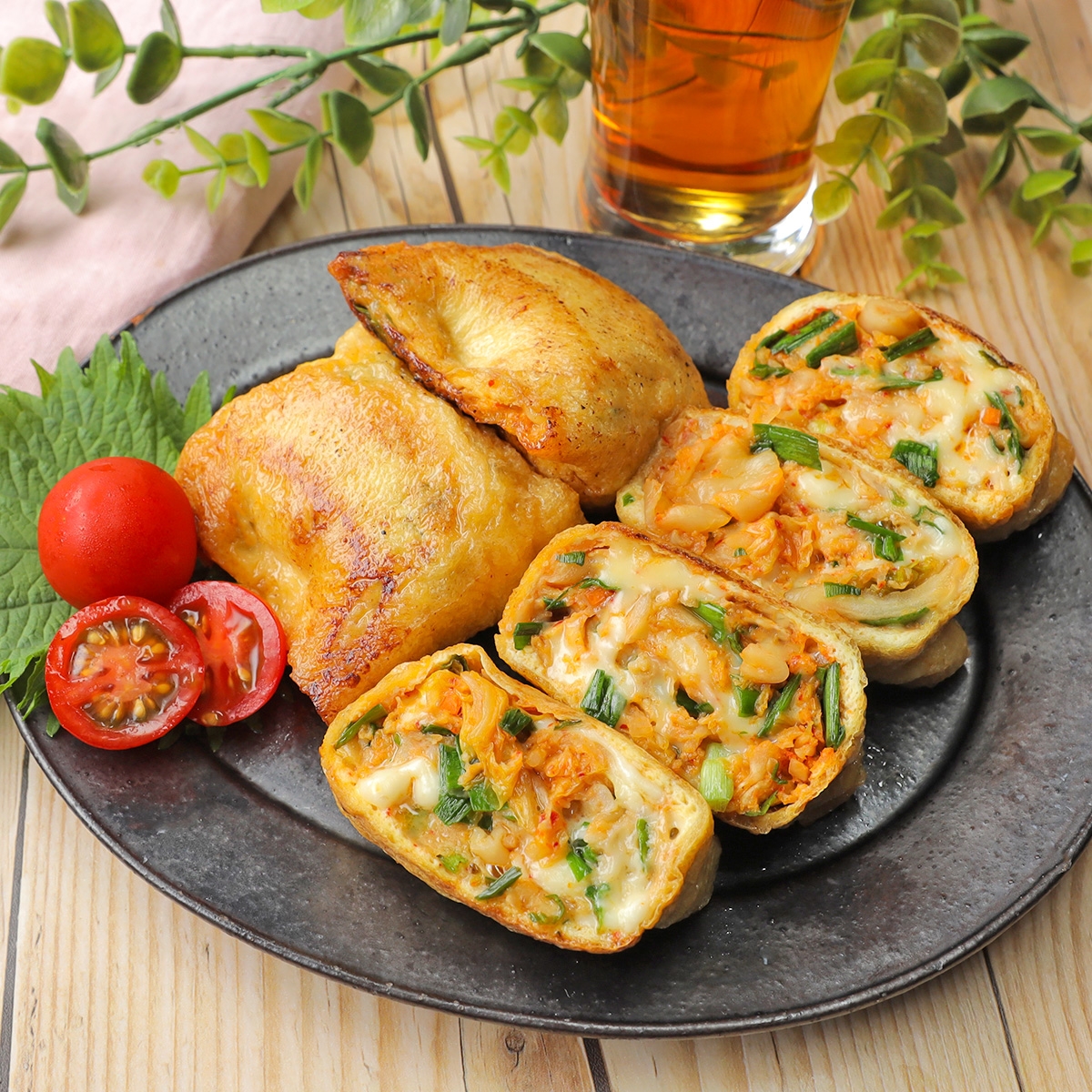 おしゃれなプレートに盛られた、おいしそうな揚げた食材と野菜ロール、横にはトマトと野菜が添えられ、後ろには飲み物があります。