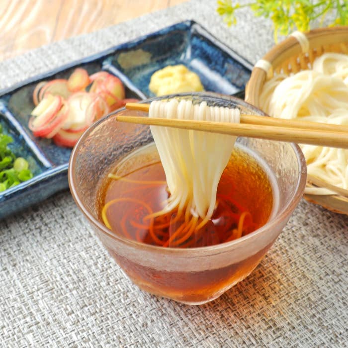 ガラスの器にめんつゆと素麺。隣に薬味と素麺が盛られたざるがある和食の場面。