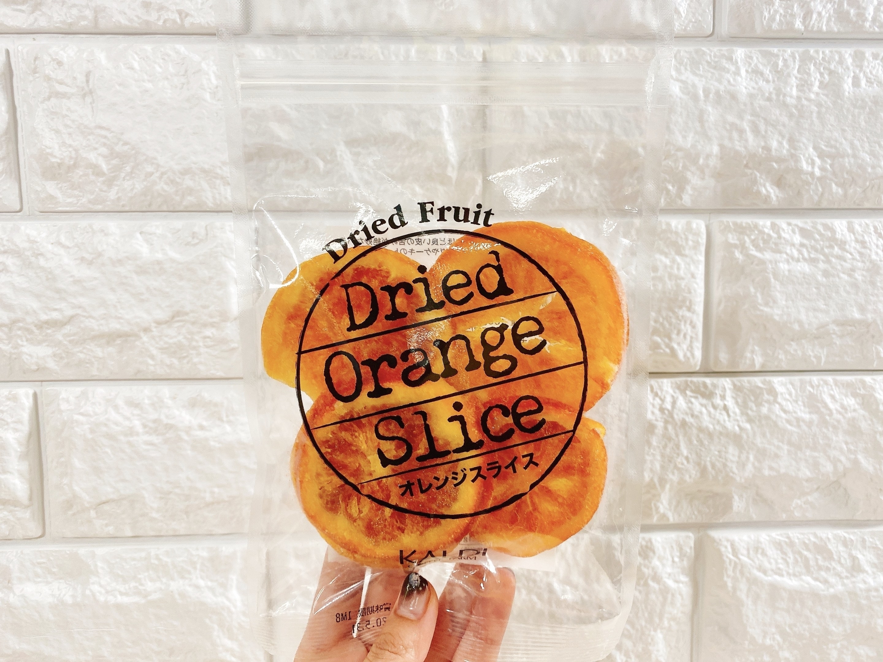 手に持たれたオレンジスライスのドライフルーツのパッケージ。表示には「Dried Orange Slice」と書かれています。
