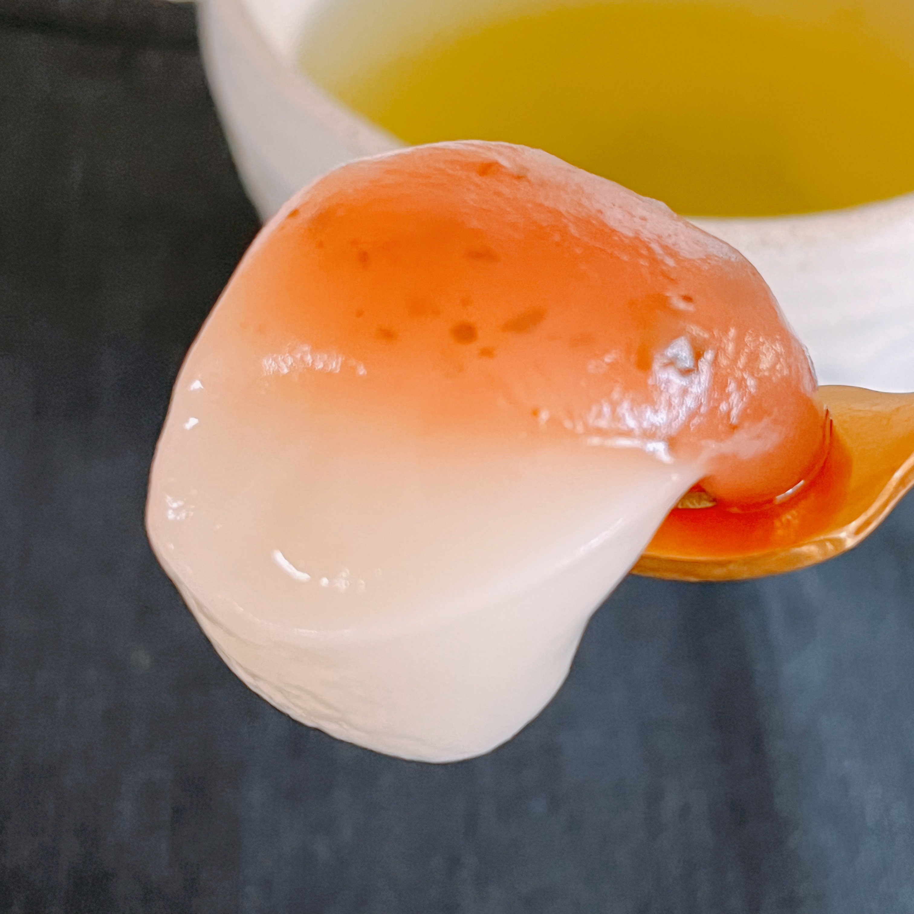 スプーンに載った白玉団子に鮮やかなソースがかかっている。背景に茶碗が見える。