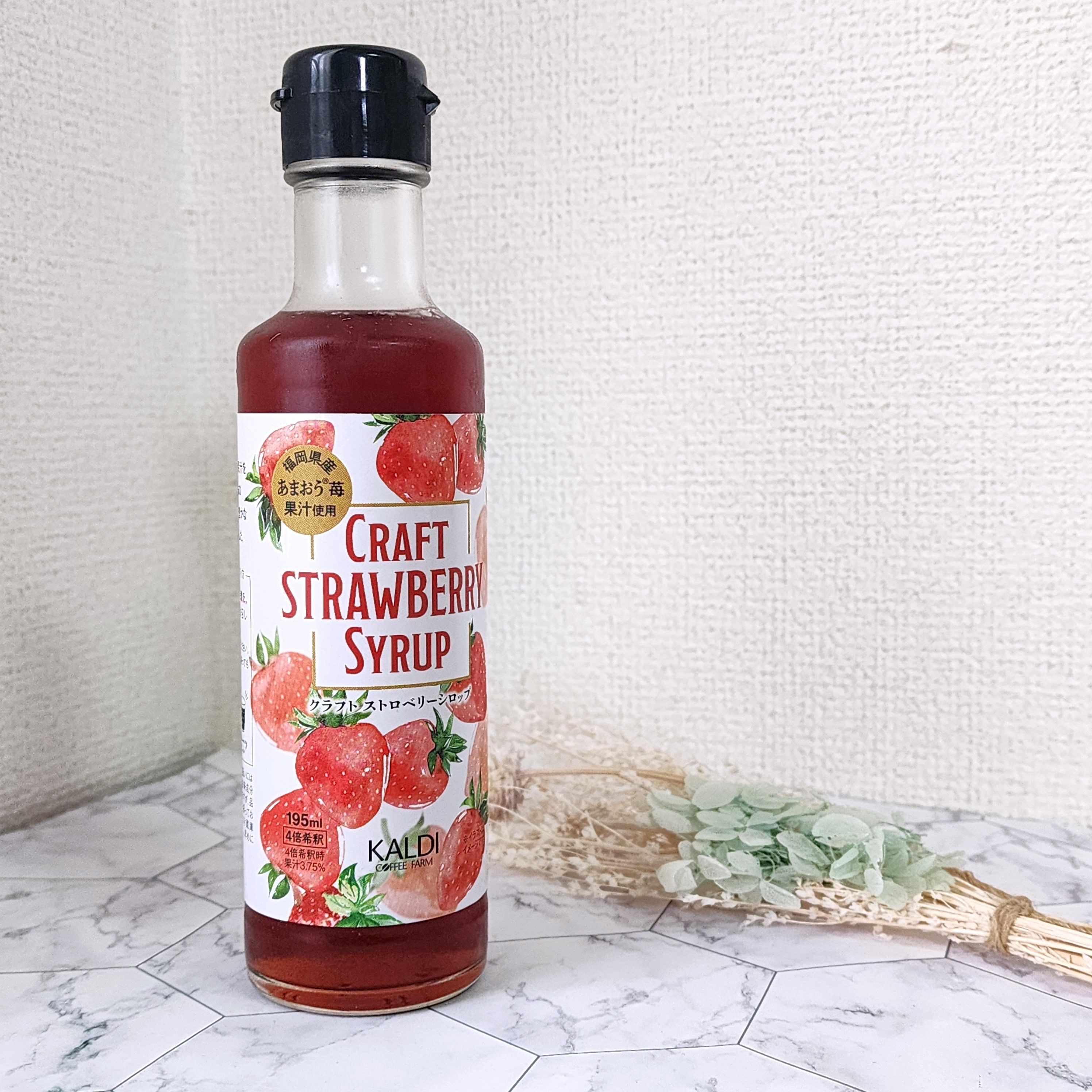 KALDIのクラフトストロベリーシロップのボトルが置かれたテーブル。背景に乾燥した植物。