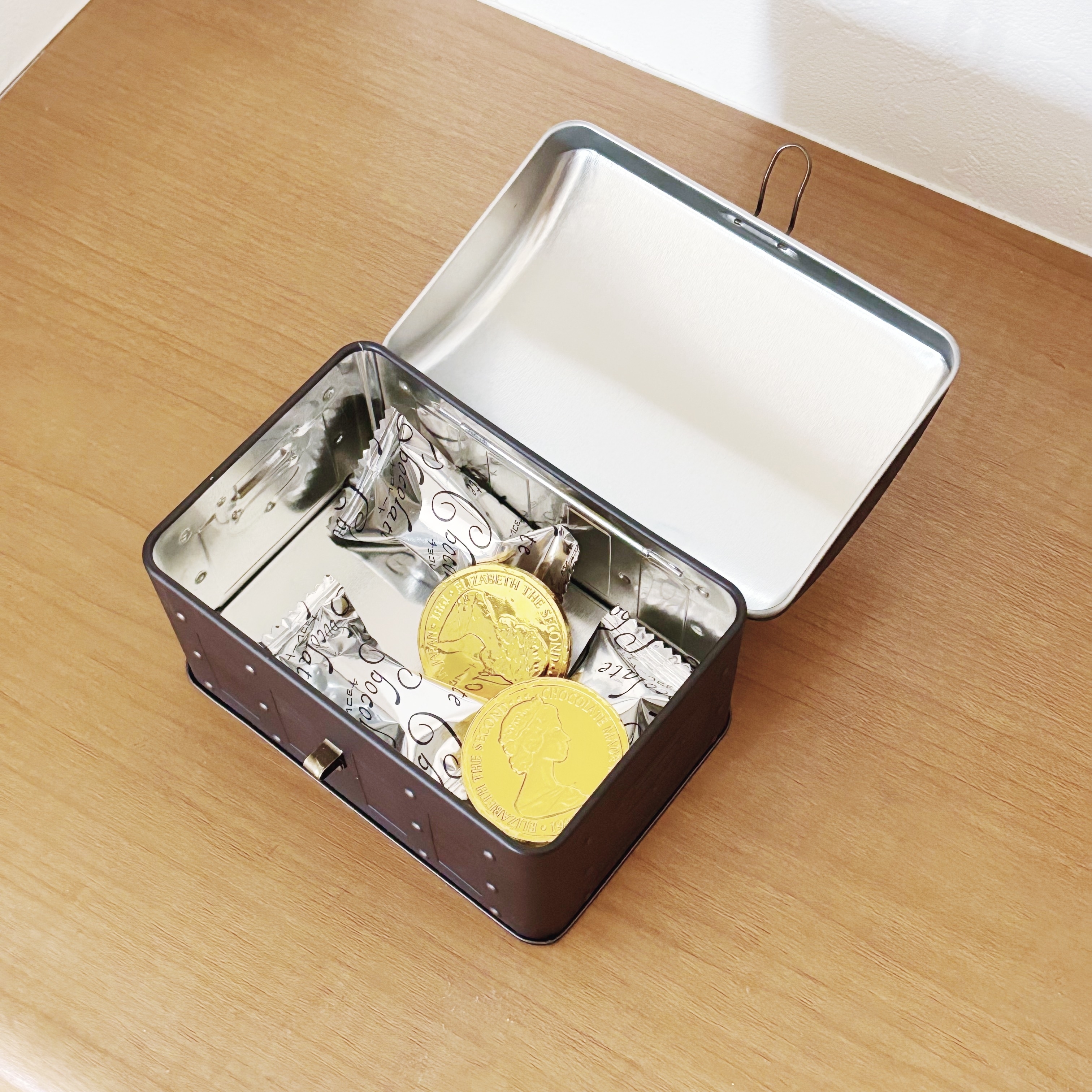 金色のコイン型チョコレートと包装されたチョコレートが入った開けられた缶の画像。