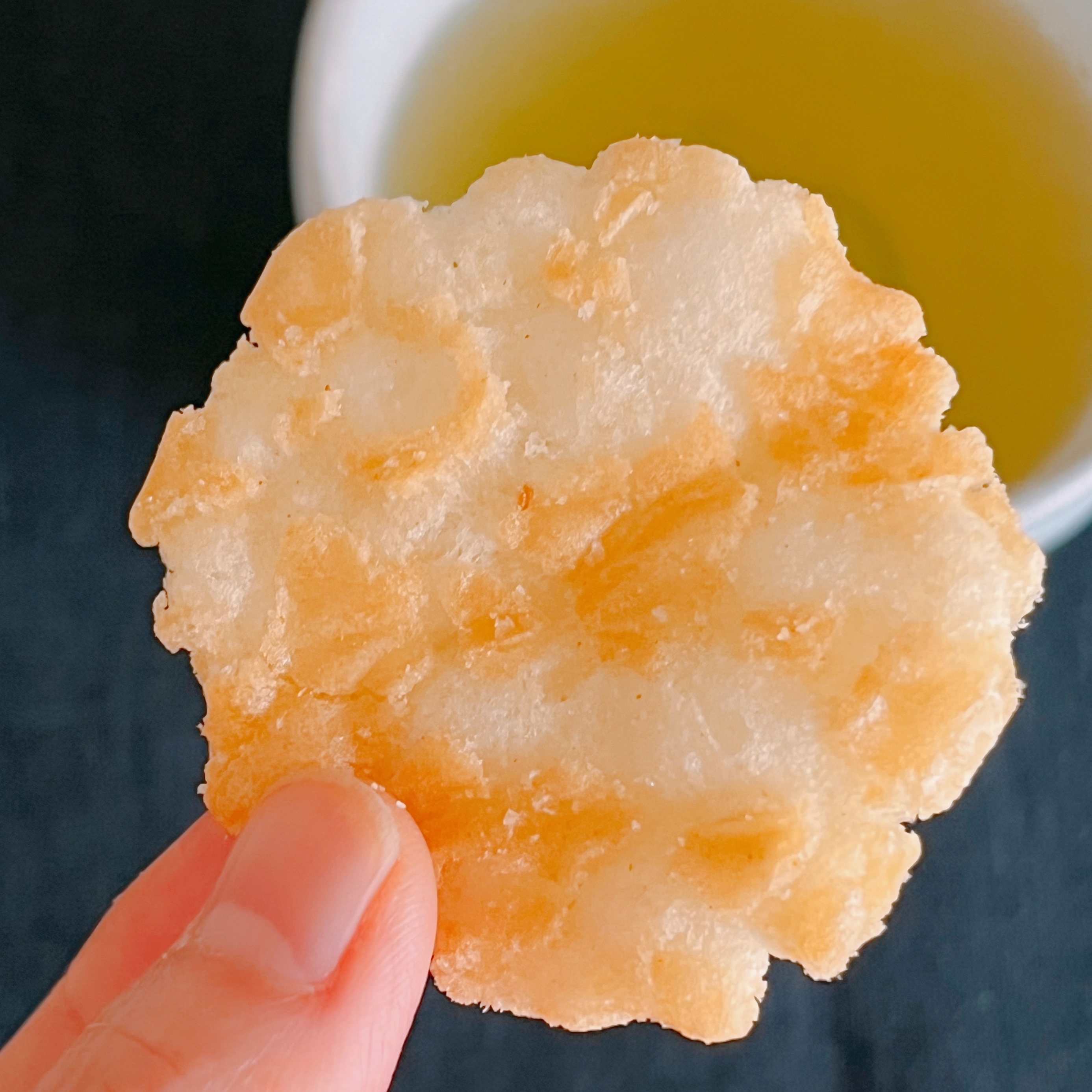 煎餅を手に持ち、お茶が背景に映っている。