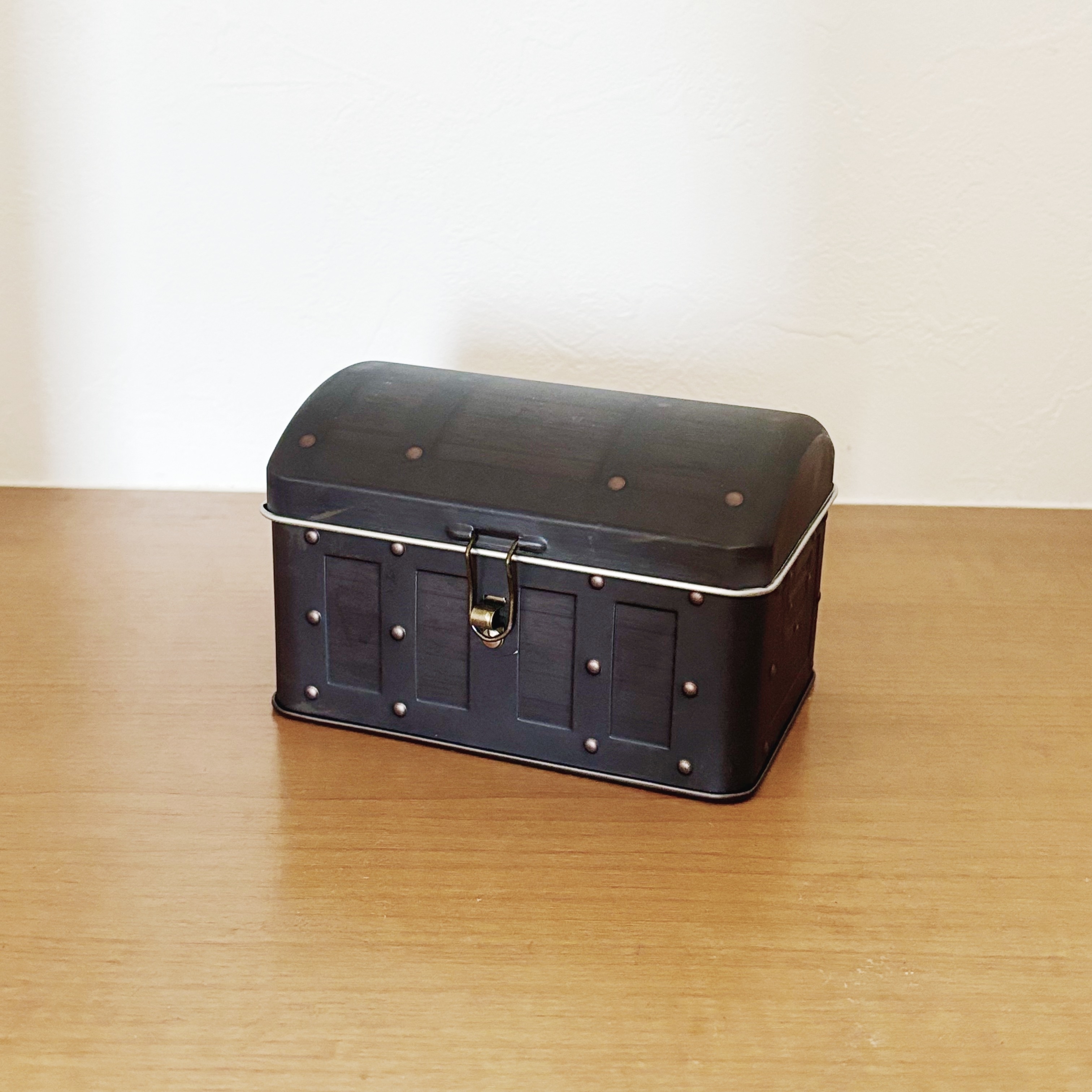 黒い金属製の宝箱型小物入れが木のテーブルに置かれている。
