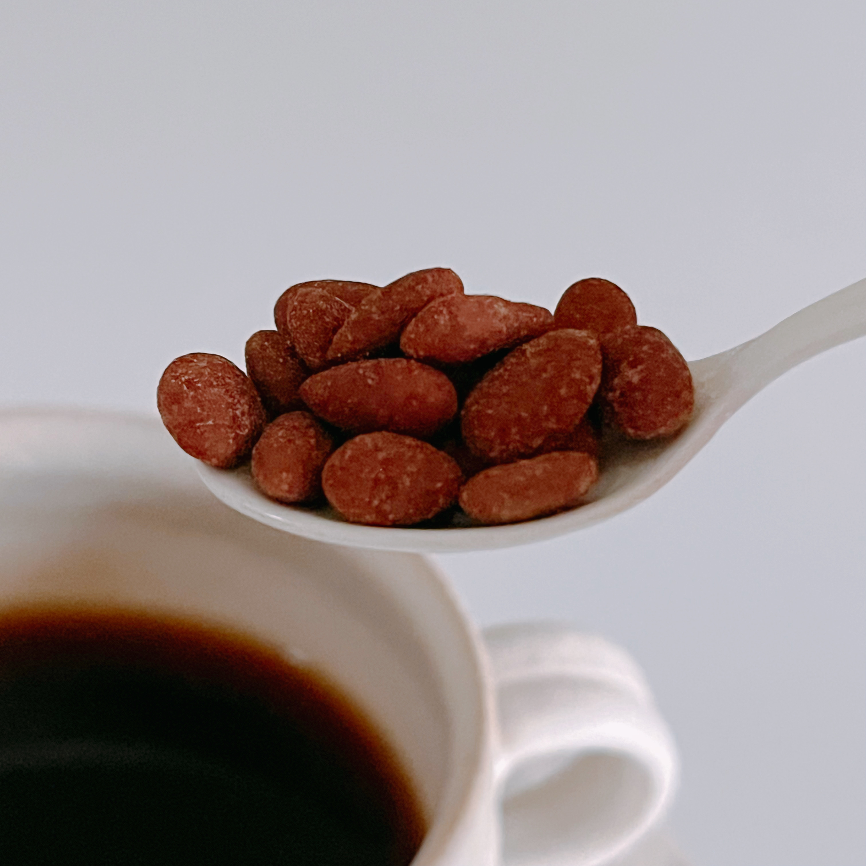 スプーンに乗ったアーモンド類の食品を持ち上げる動作とコーヒーカップ。