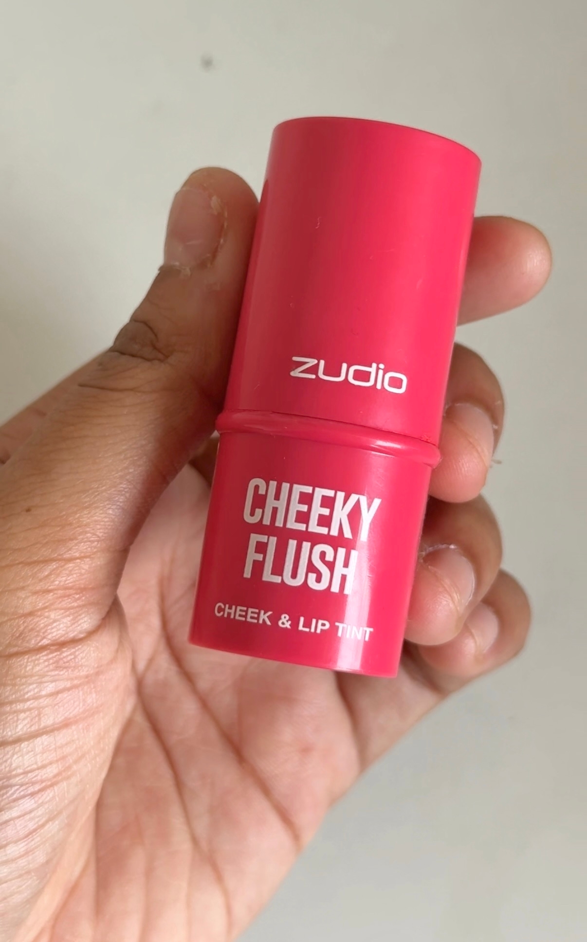 Hand holding a tube of Zudio Cheeky Flush, a cheek and lip tint product