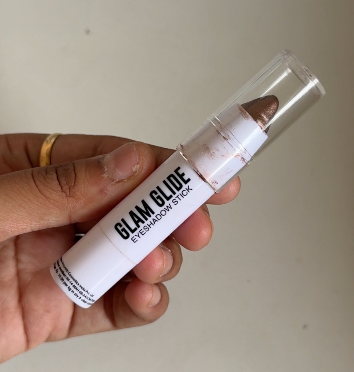 Hand holding a Glam Glide eyeshadow stick, shown in close-up, with a clear cap displaying the makeup tip