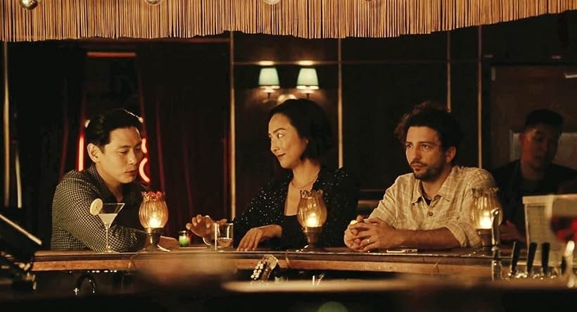 Three people sitting at a dimly lit bar, engaging in conversation. They are dressed in casual, stylish attire