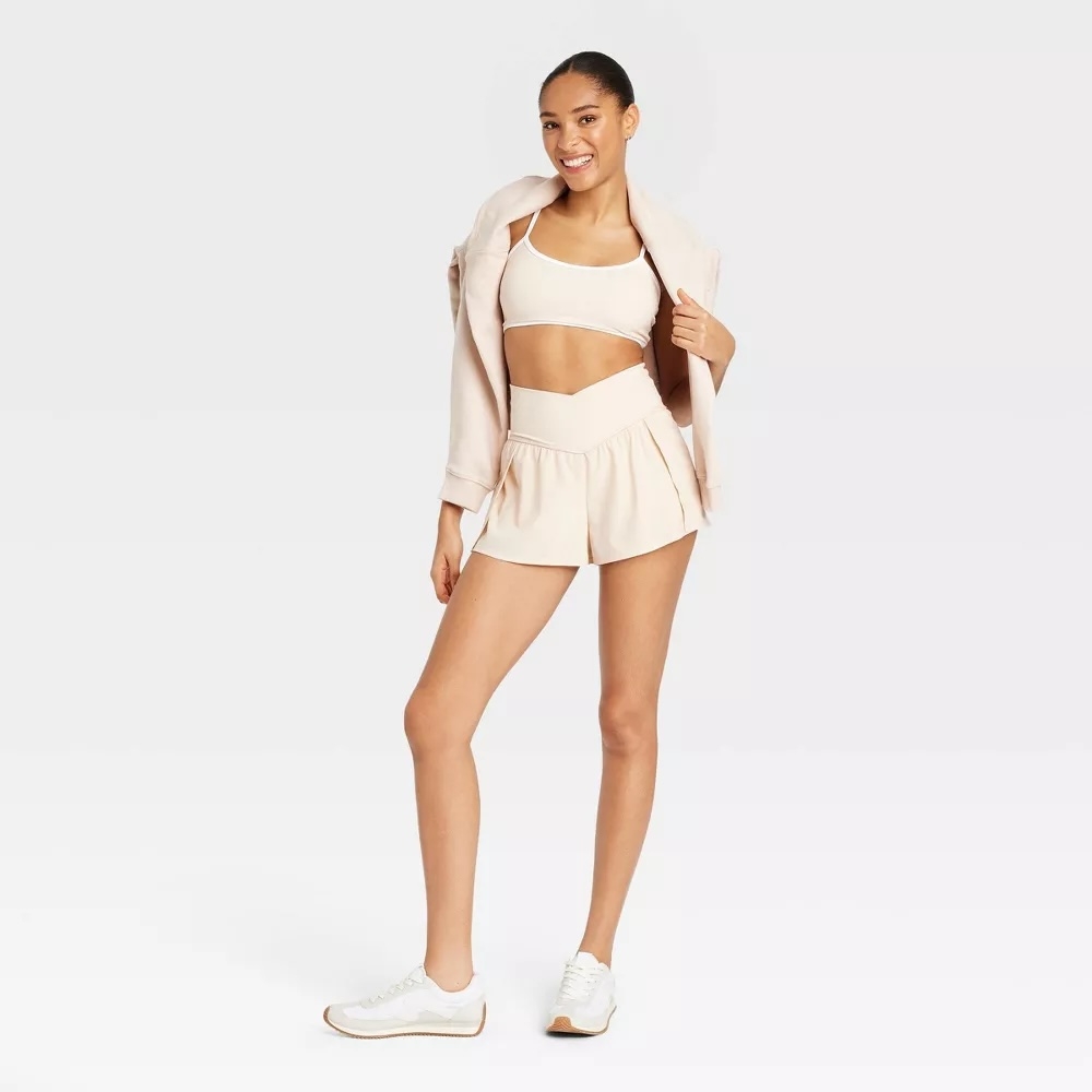 Model wearing a casual outfit: a crop top, shorts, jacket, and sneakers, posing for a shopping article