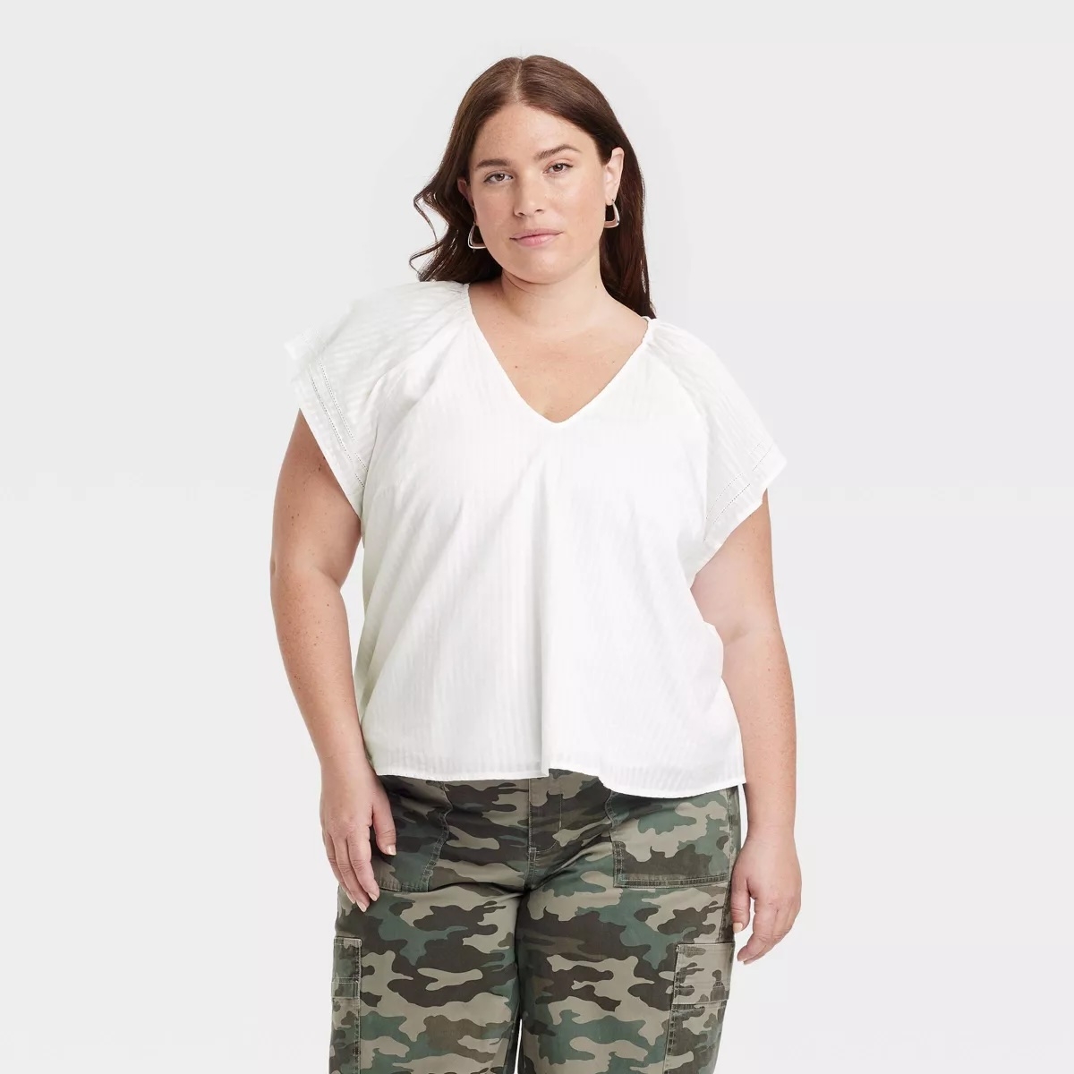 Person in a casual outfit with a white top and camouflage pants, standing confidently