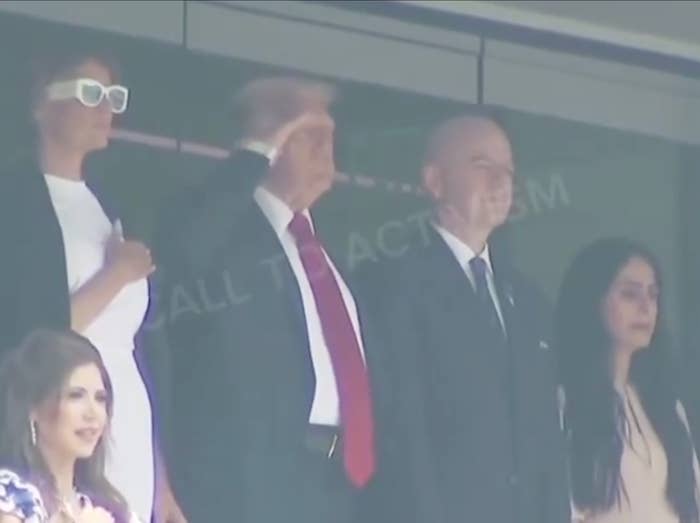 A man and others stand in a balcony, with the man saluting. One woman is in a white outfit with white-framed sunglasses