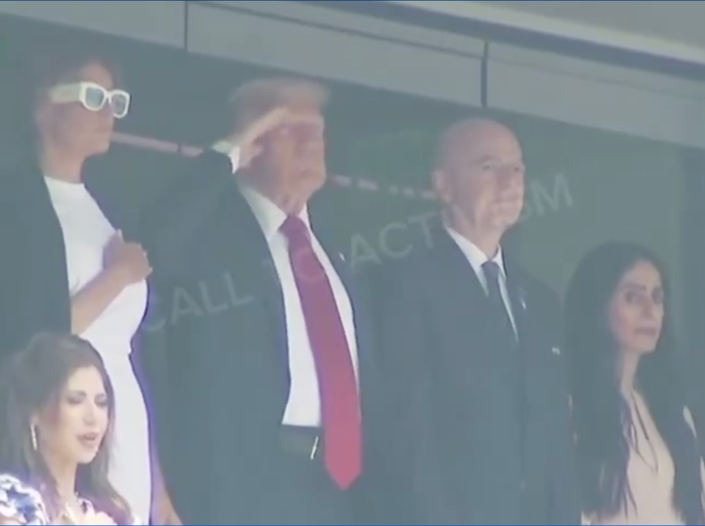 A group of people stand on a balcony. One man salutes while others stand beside him. They are attending an event, dressed in formal attire