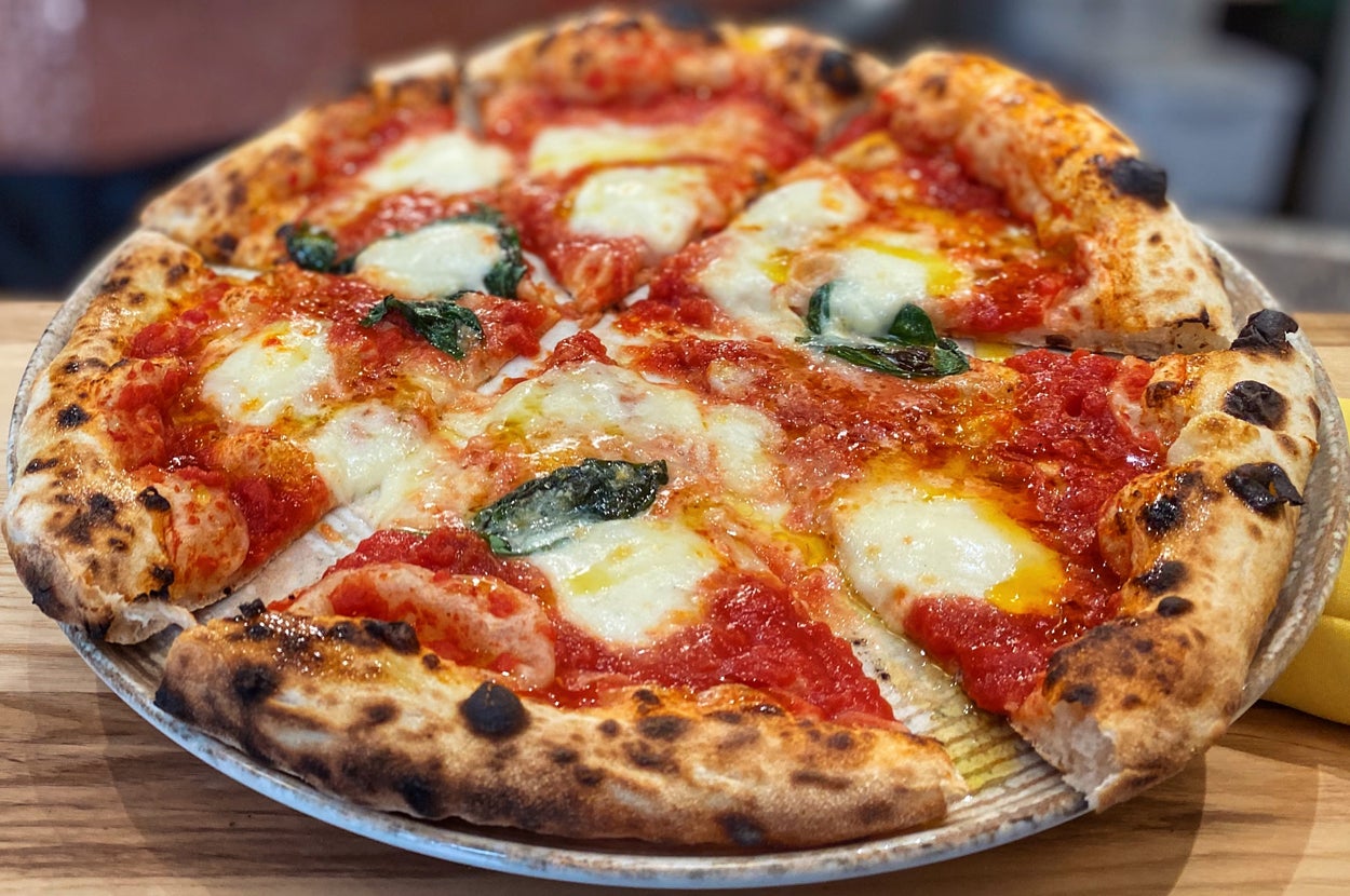 Close-up of a freshly baked Margherita pizza with melted mozzarella, tomato sauce, and basil leaves on a wooden table