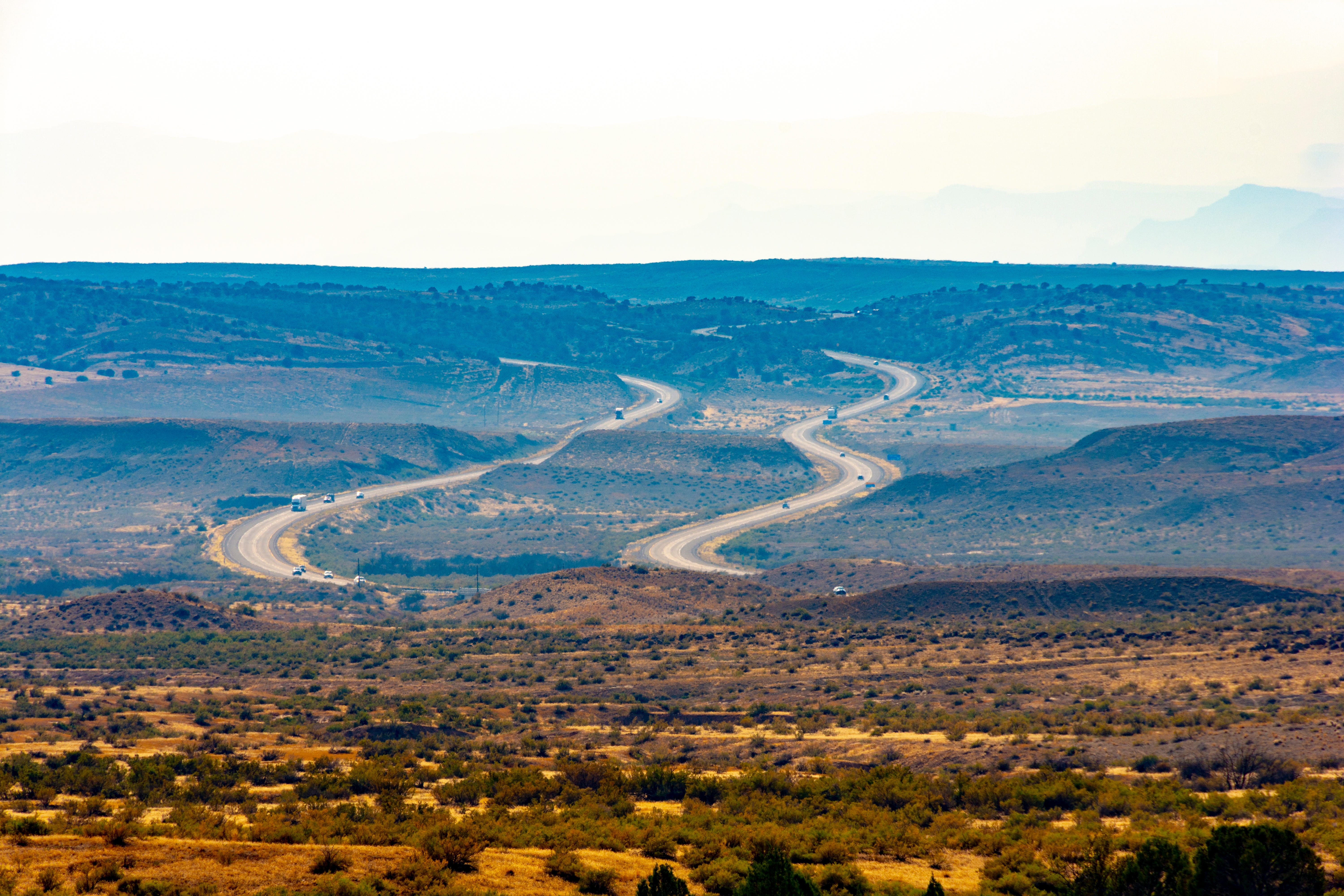 A winding road stretches through a vast, open desert landscape under a clear sky