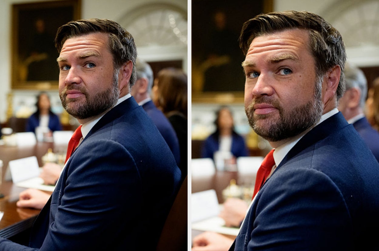 Vance in a suit and tie looks over his shoulder during a formal meeting in a conference room
