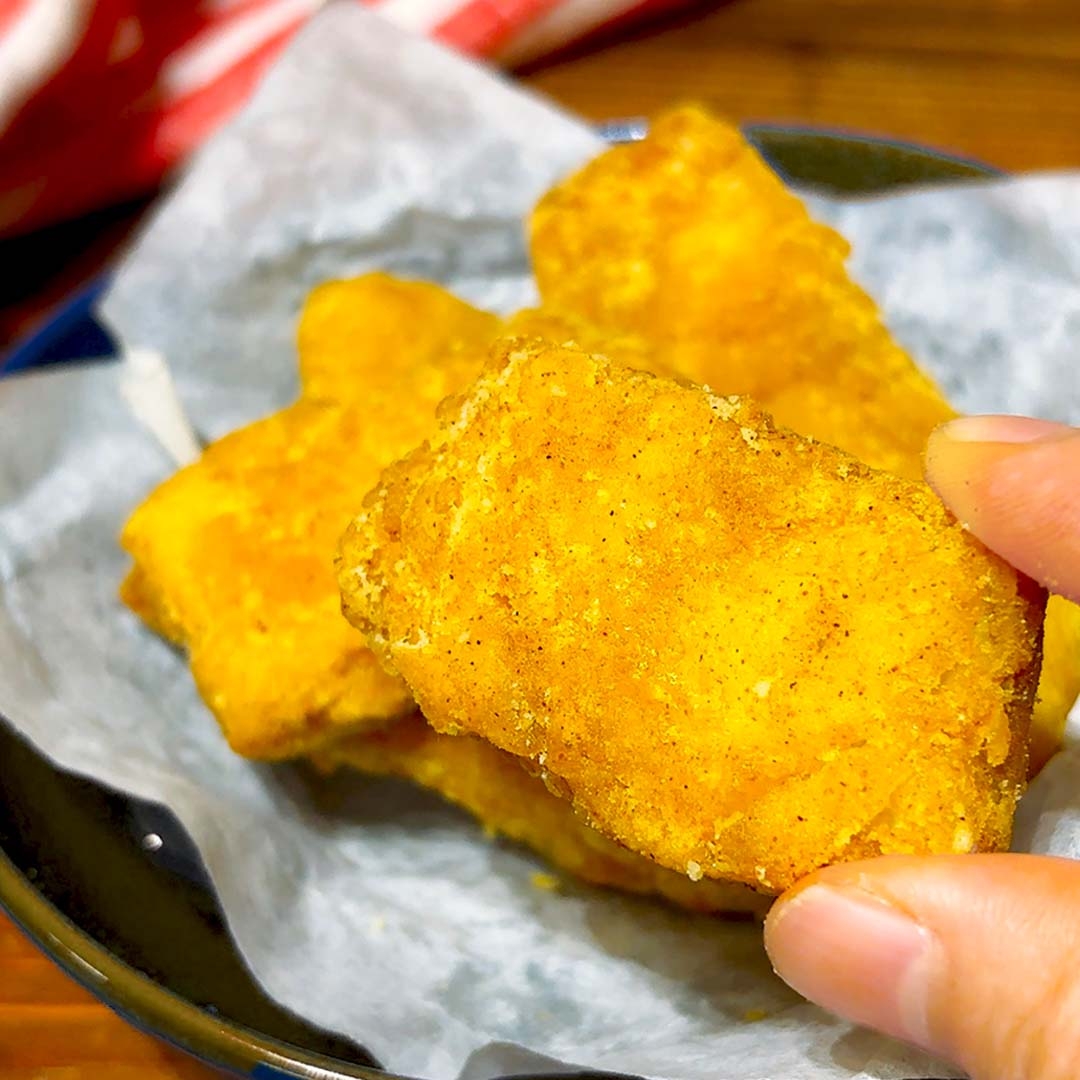 手でつかまれた揚げたチキンナゲットのクローズアップショット。お皿に数個盛られている。