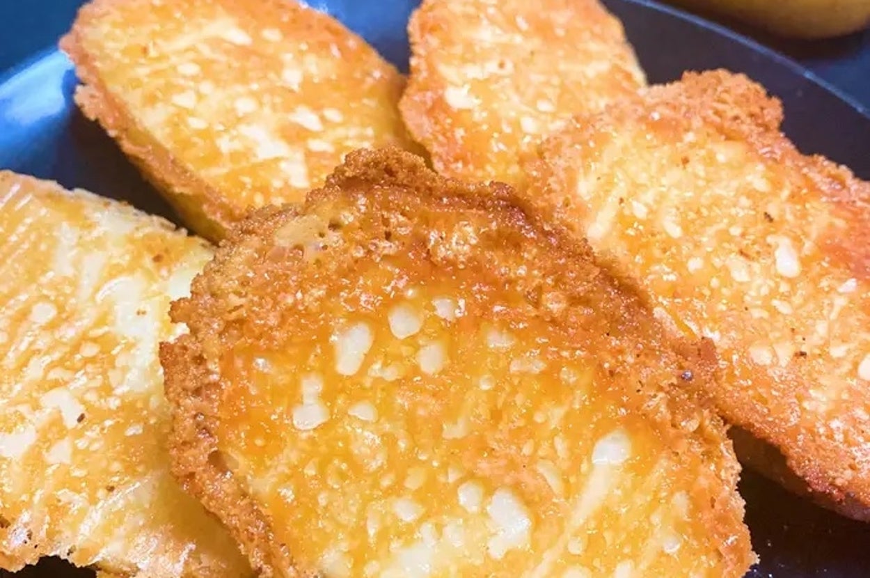 カリカリに揚げられたポテトチップスが皿にのっている。背景に数個のじゃがいもが見える。
