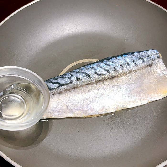 フライパンにさばの切り身と小さなカップに入った液体。料理の準備段階を示しています。