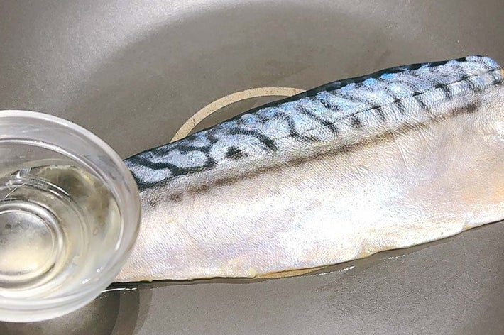 フライパンに置かれたサバの切り身と小さなカップに入った液体。調理の準備段階を示す。