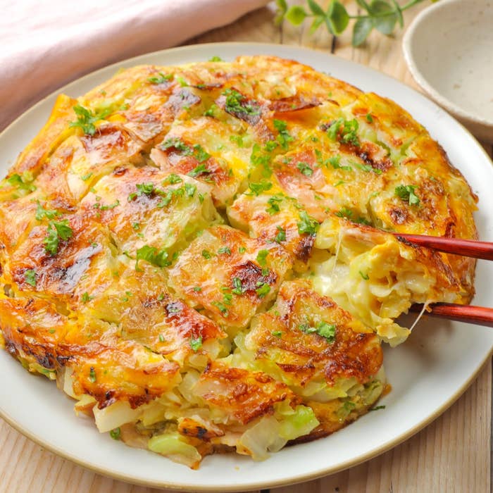 料理が皿に盛られ、箸で持ち上げられている。キャベツが具材として見える。