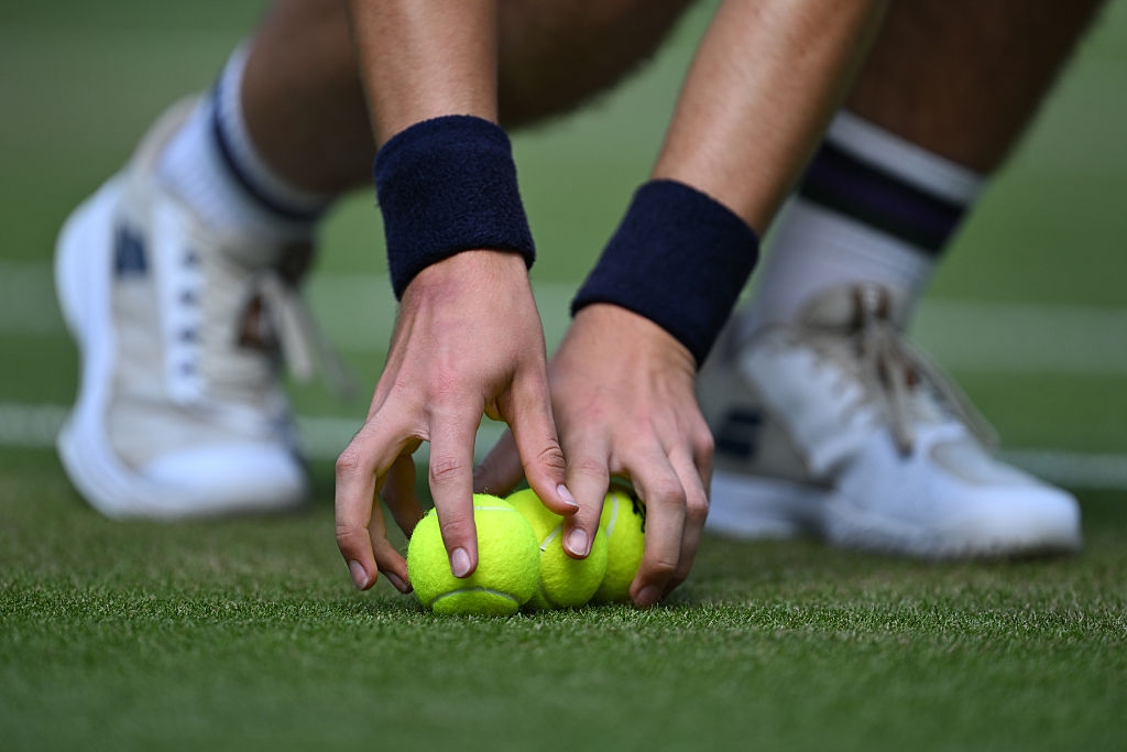 Hands picking tennis balls from grass court, wearing wristbands and sneakers
