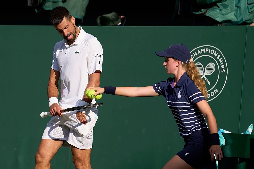 A tennis player receives a ball from a ball girl during a match, both focused and prepared for play