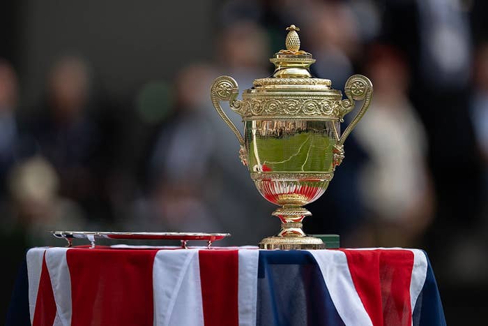 A gold tennis trophy and a silver tray on a table draped with a Union Jack-themed cloth, in an outdoor setting