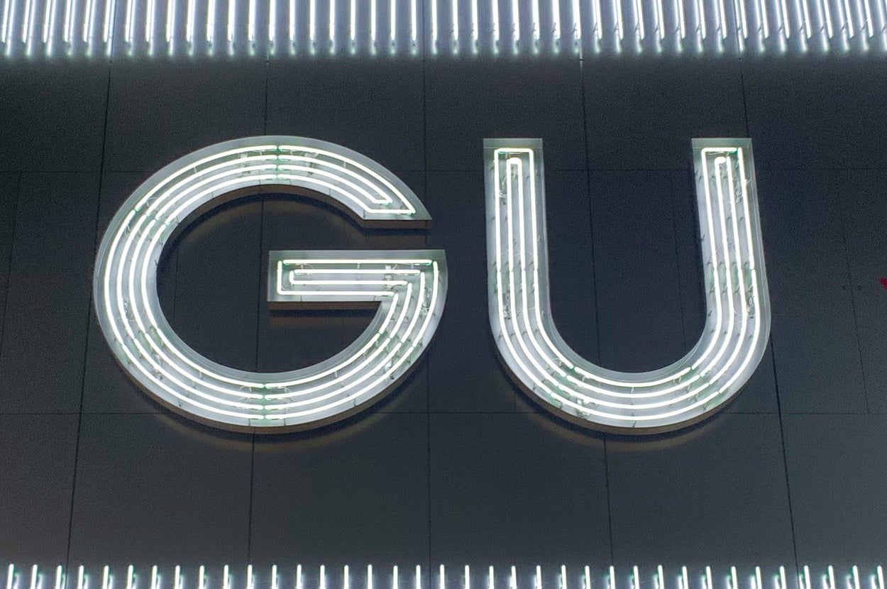 Illuminated GU sign on a wall, framed by vertical lights