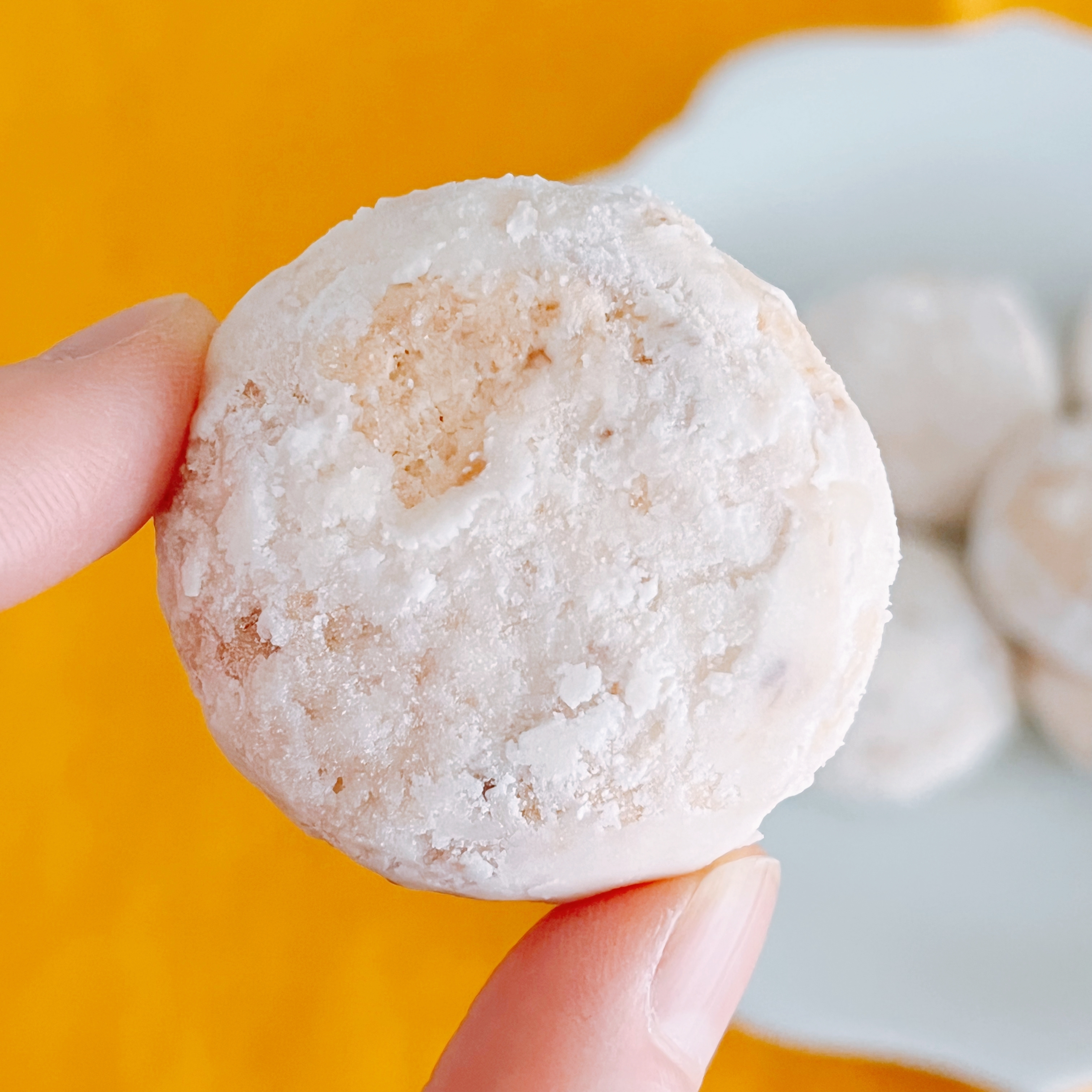 手に持たれた粉砂糖がまぶされたクッキー。背景に同様のクッキーが4枚見える。